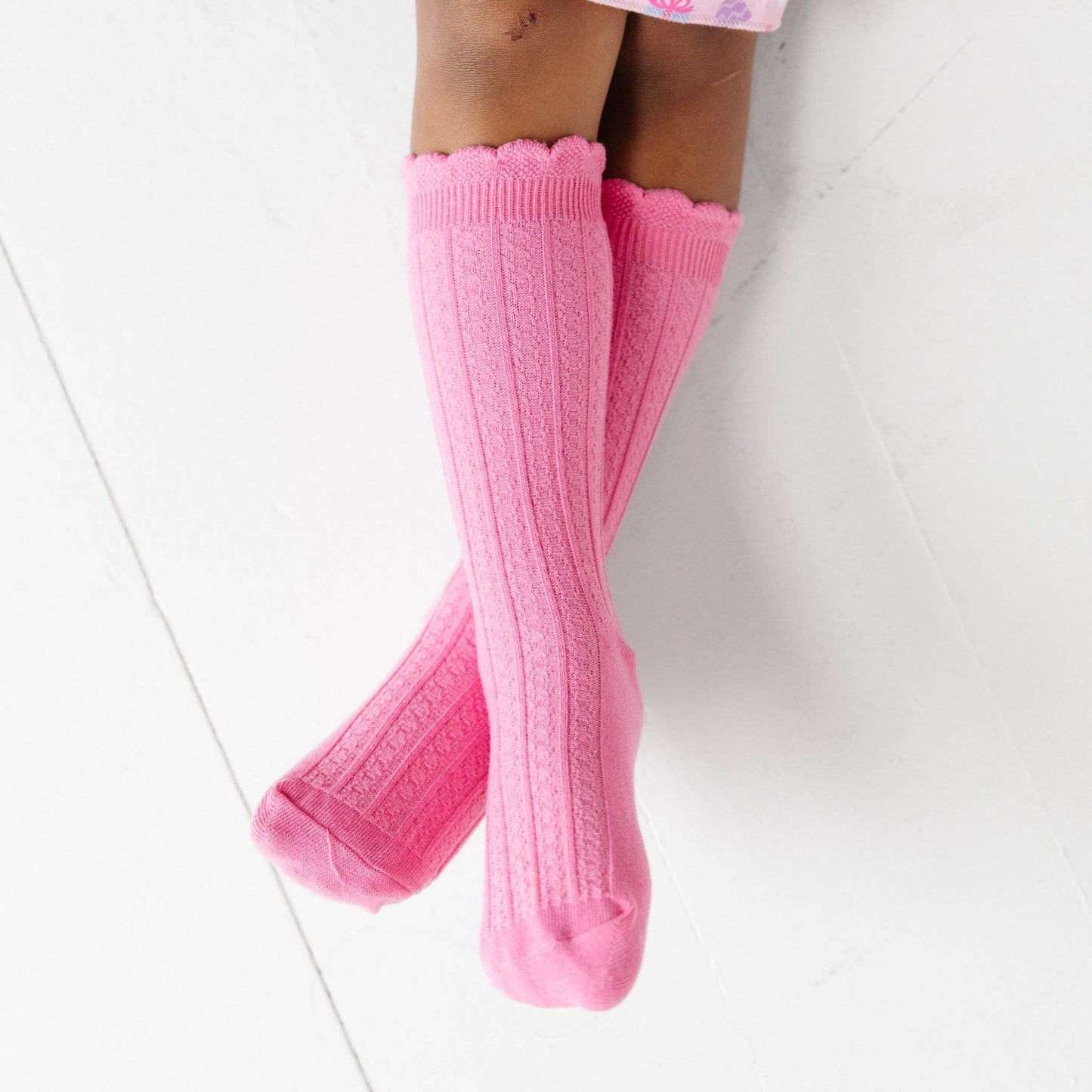 Pink knee-high socks with scalloped edges on a white background