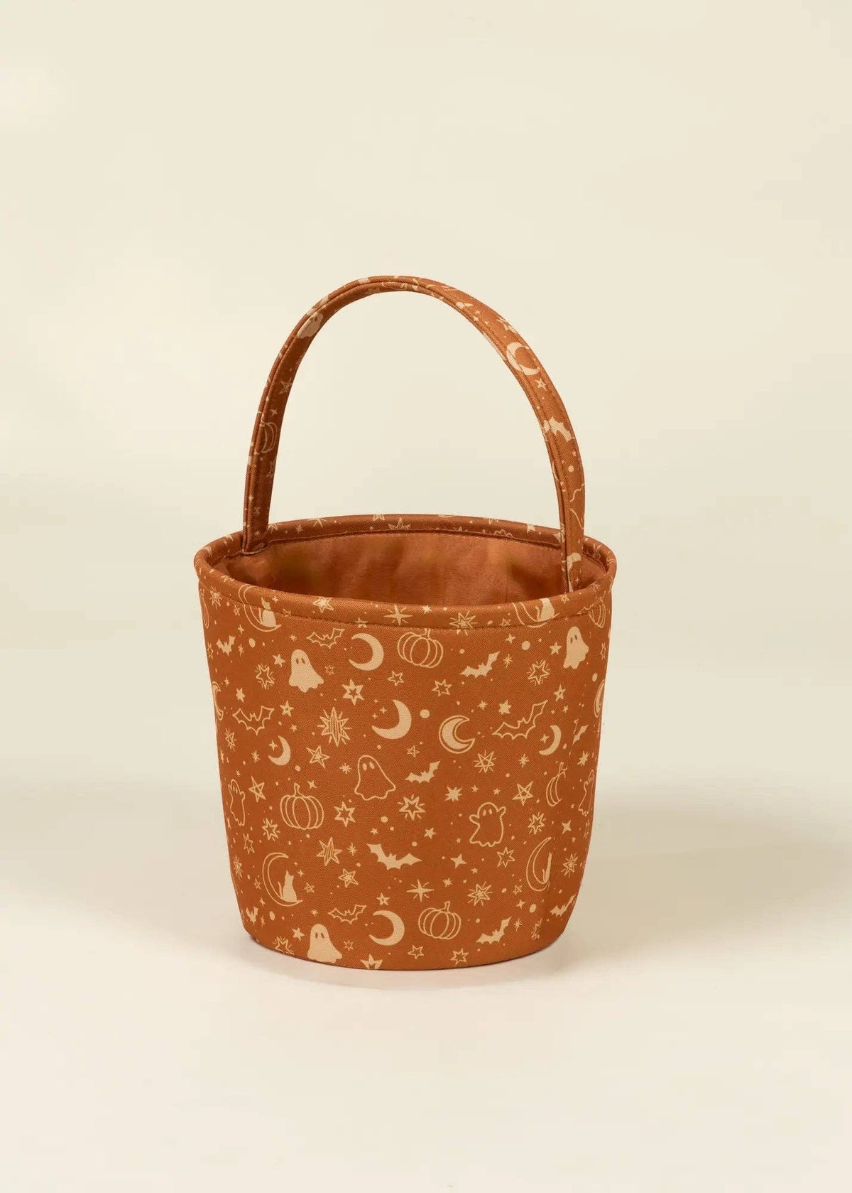 A small fabric bucket-style tote bag with a curved top handle, featuring a warm rust-orange base color covered in a cream-colored celestial and autumn pattern of moons, stars, pumpkins, and ghosts, set against a plain off-white background.