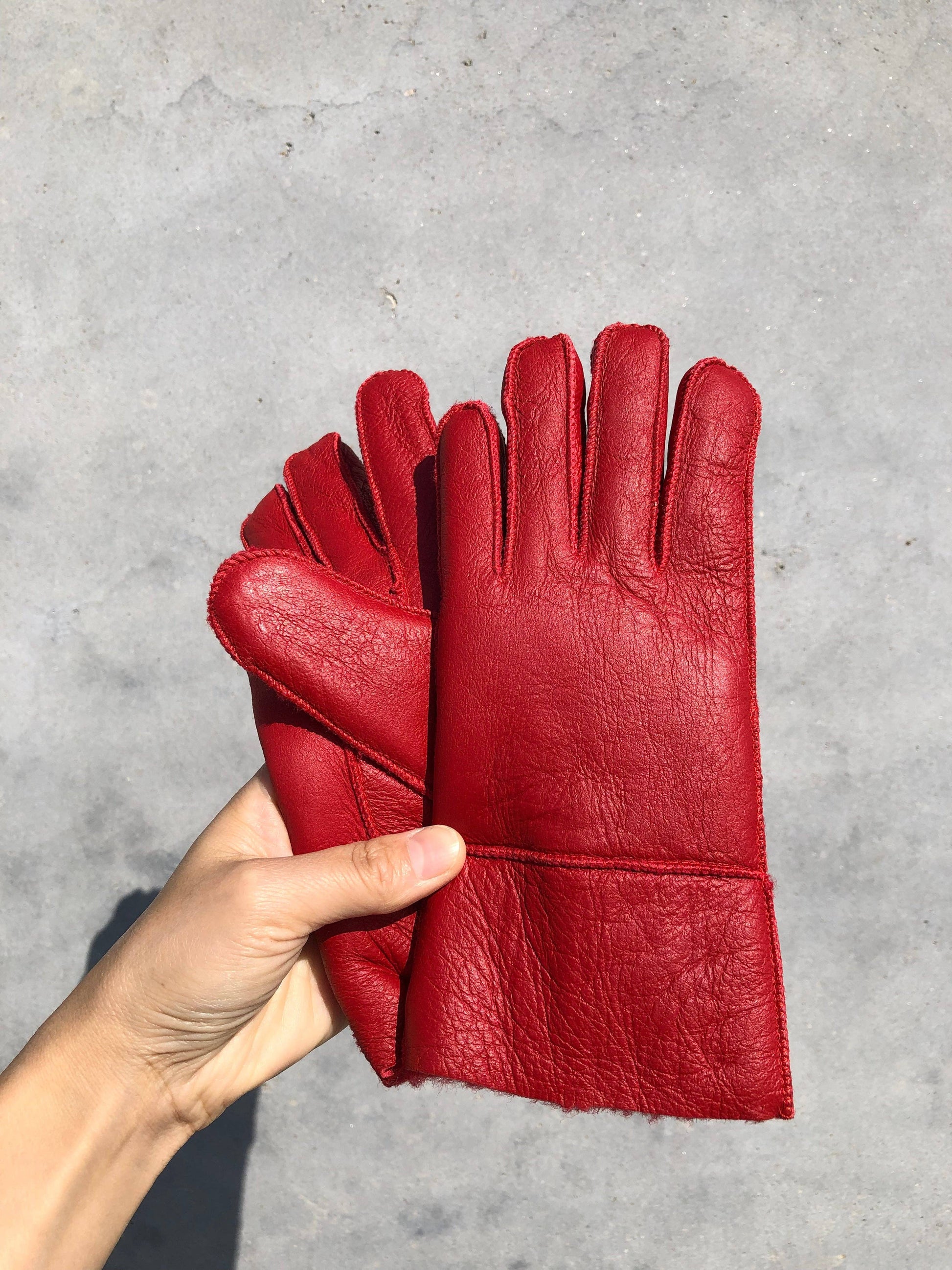 Red leather gloves held by a hand on a gray concrete background