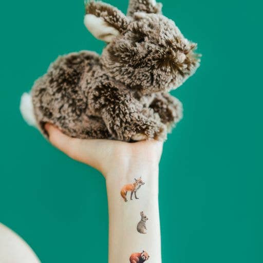 Plush rabbit toy on a hand with animal tattoos against a teal background