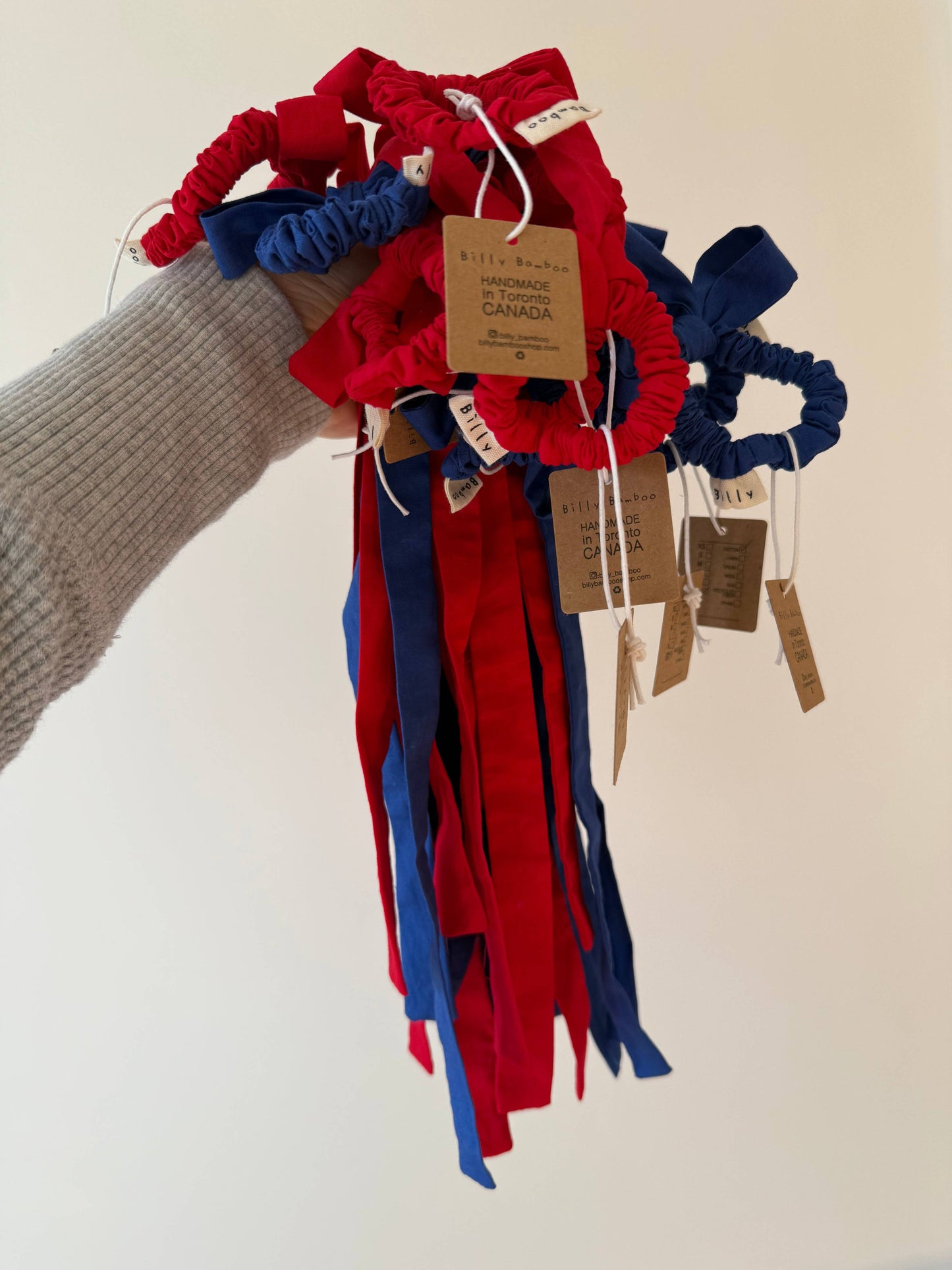 Red and blue hair ties with tags held by a person wearing a gray sweater.