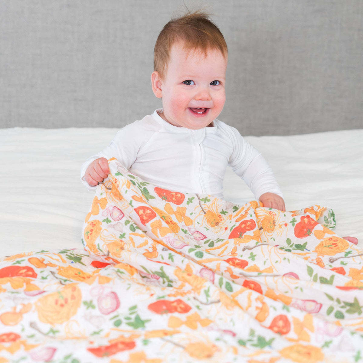 Baby holding a pasta print blanket on a bed