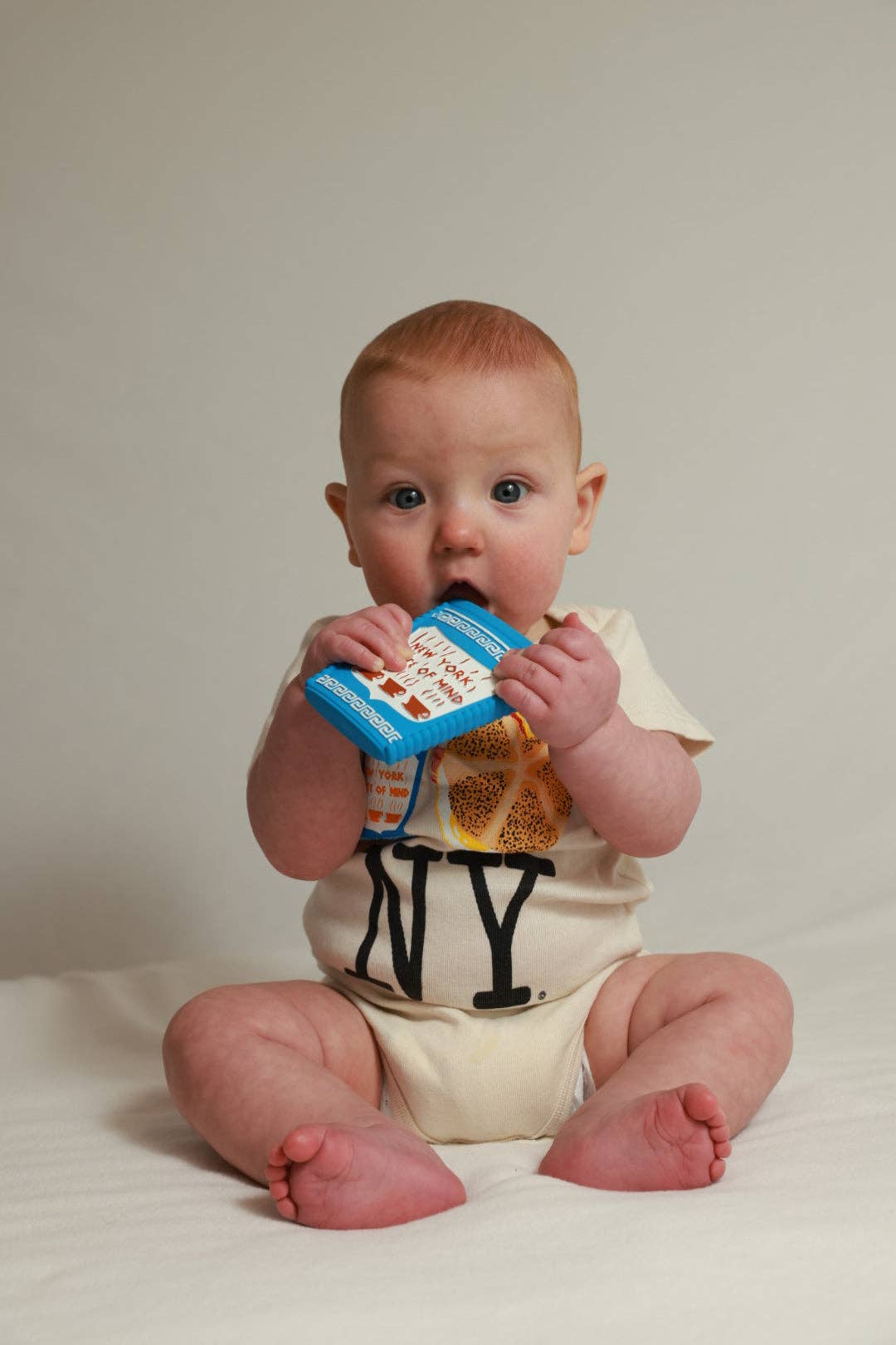 Baby holding a colorful teether against a plain background
