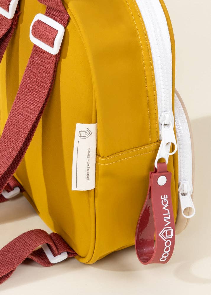Yellow bag with red strap and 'Coco Village' tag on a beige background