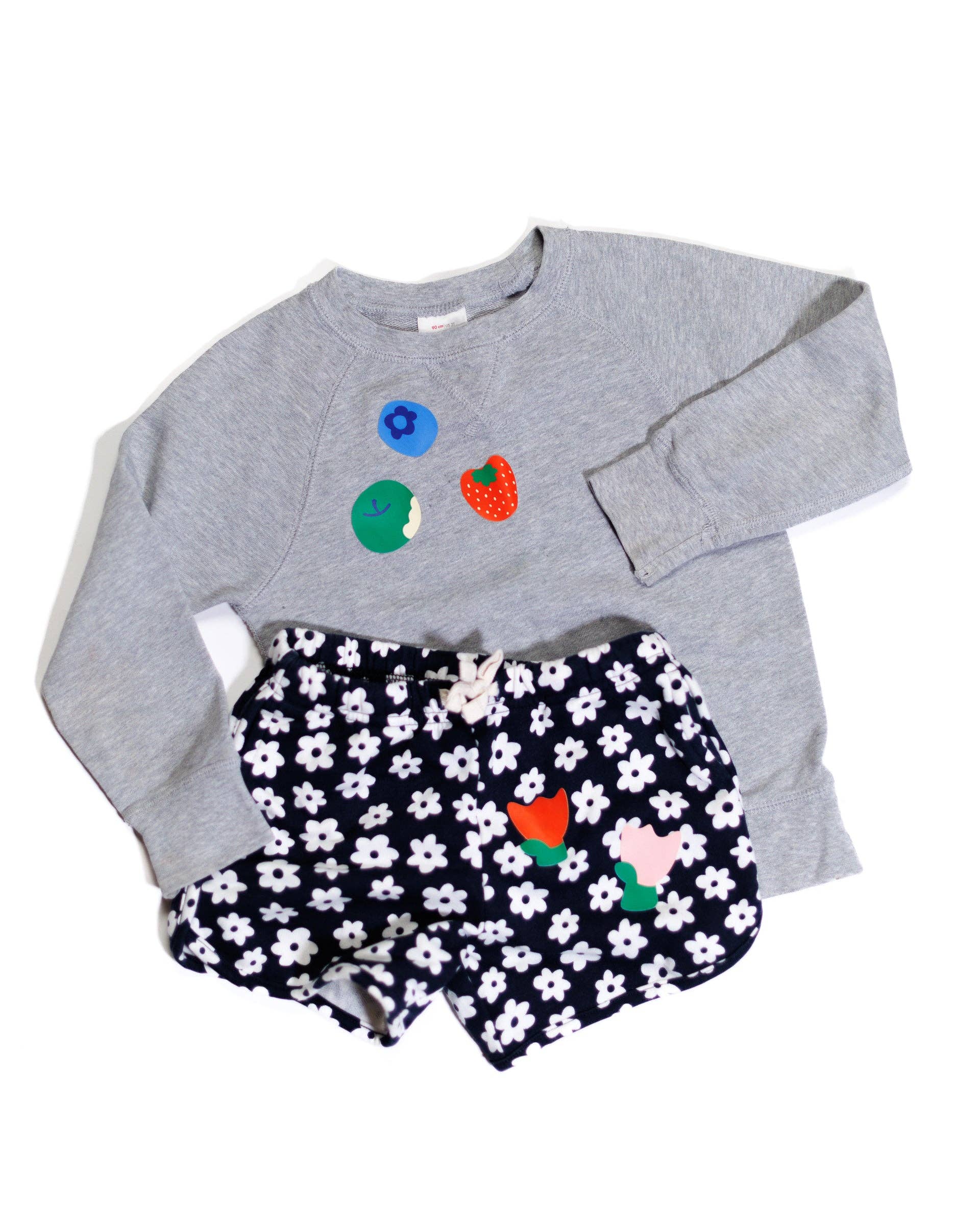 Gray sweatshirt with colorful designs and navy shorts with white floral pattern on a white background