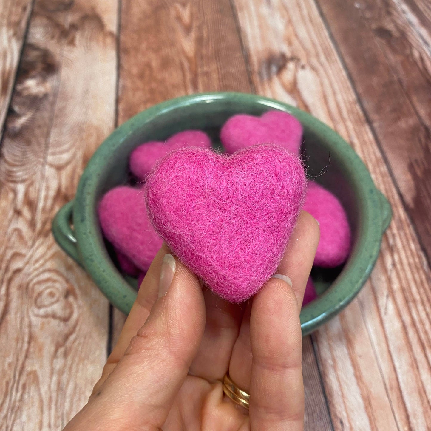 Pink heart-shaped object held by a hand over a green container on a wooden surface