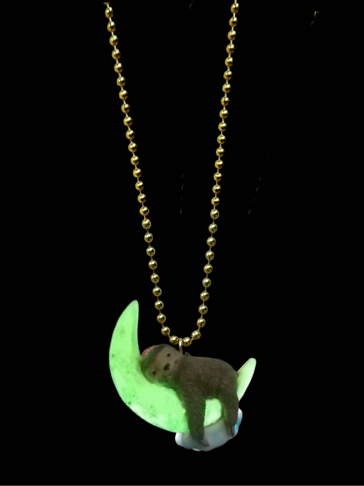 Necklace with a sloth on a moon pendant glowing in the dark against a black background