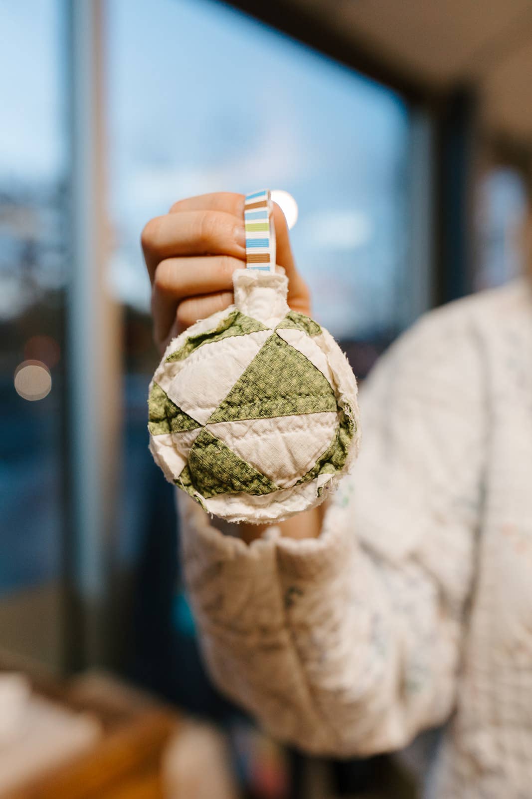 Person holding a green and white quilted ornament with a blurred background