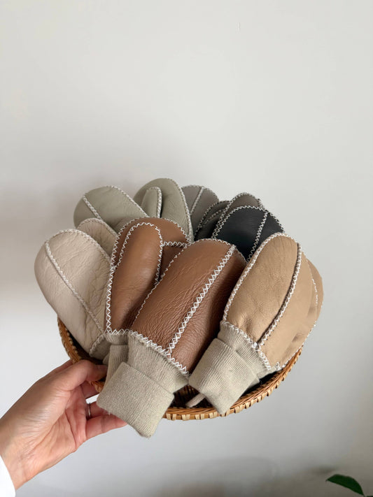 Set of leatheer mittens in various colors held in a hand against a white background