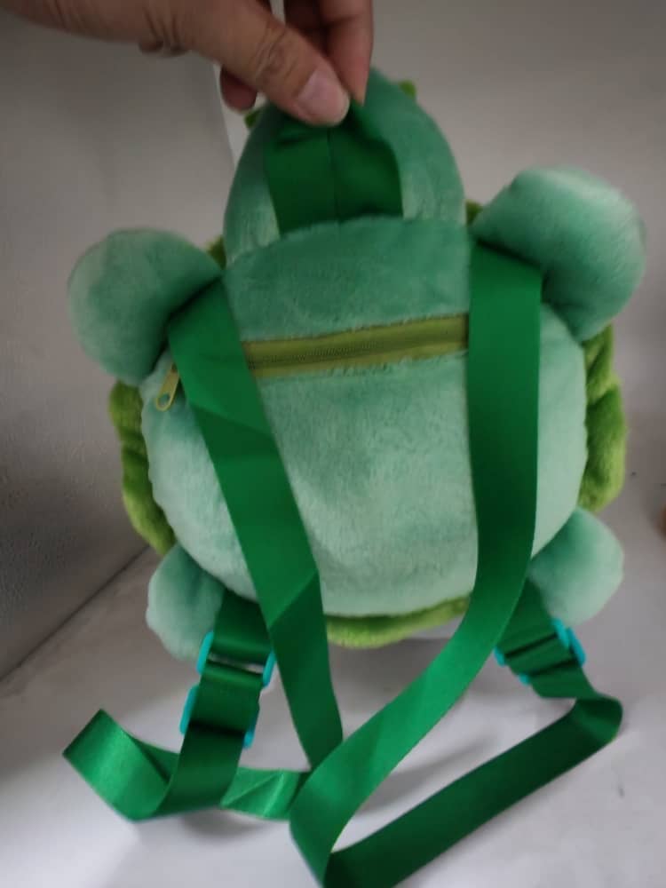 Green plush backpack held by a hand against a white background