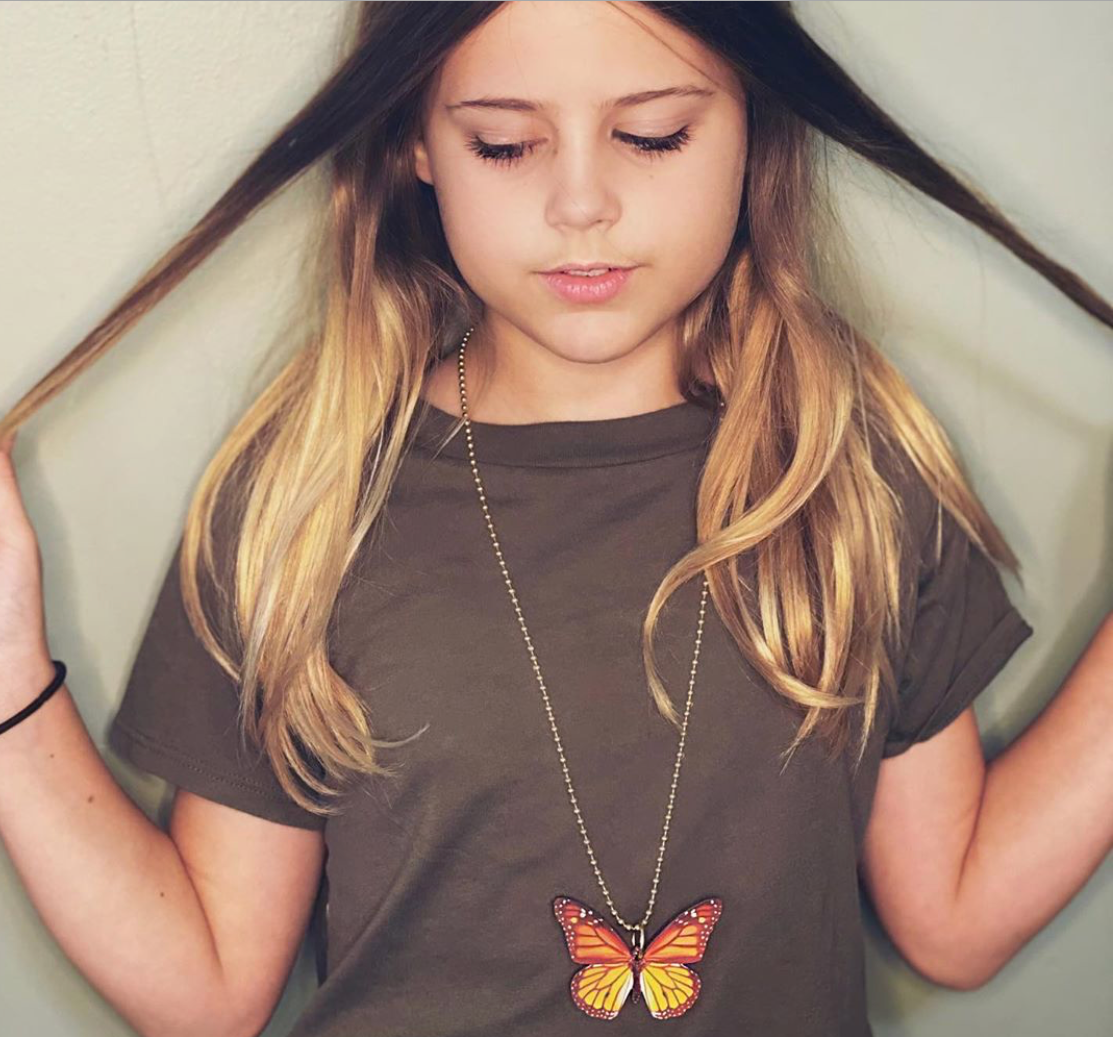 Young girl wearing a brown t-shirt with a butterfly design and a necklace.