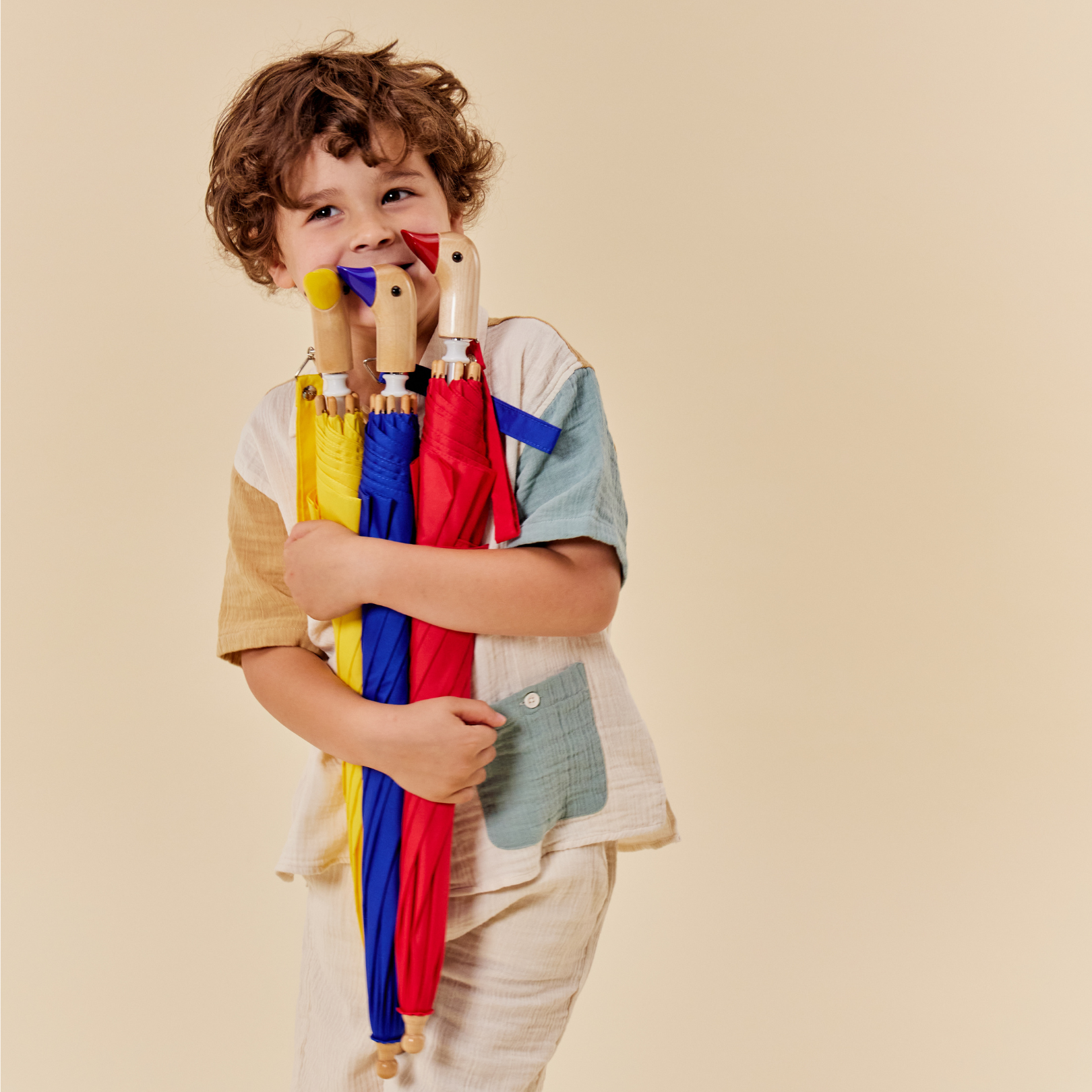 Child holding colorful umbrellas against a beige background