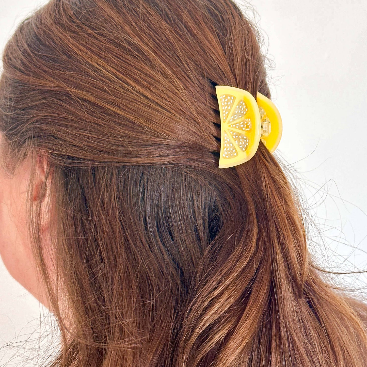 Person with brown hair wearing a yellow hair clip with decorative elements.