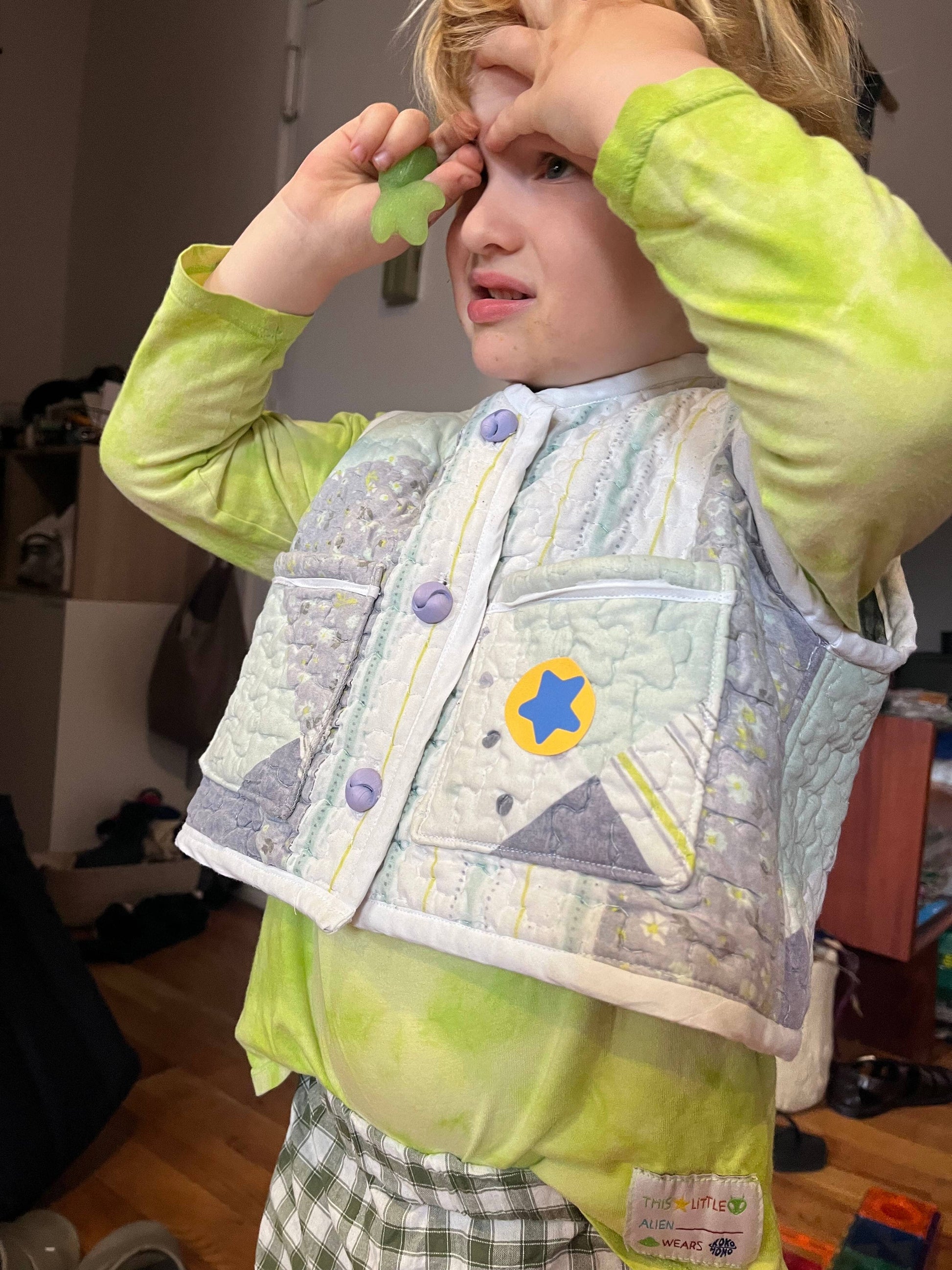 Child wearing a green jacket and patterned vest indoors