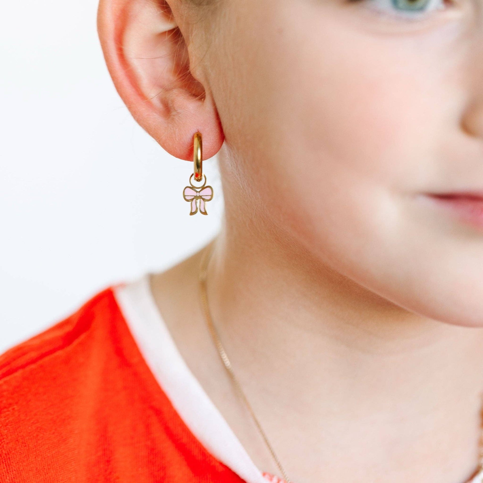 Close-up of a child wearing gold bow-shaped earrings with a plain background.