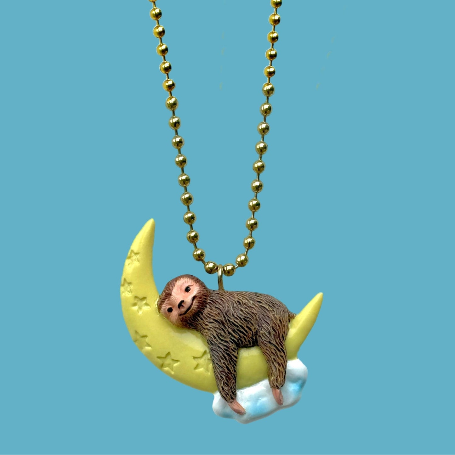 Necklace with sloth on a moon pendant against a blue background