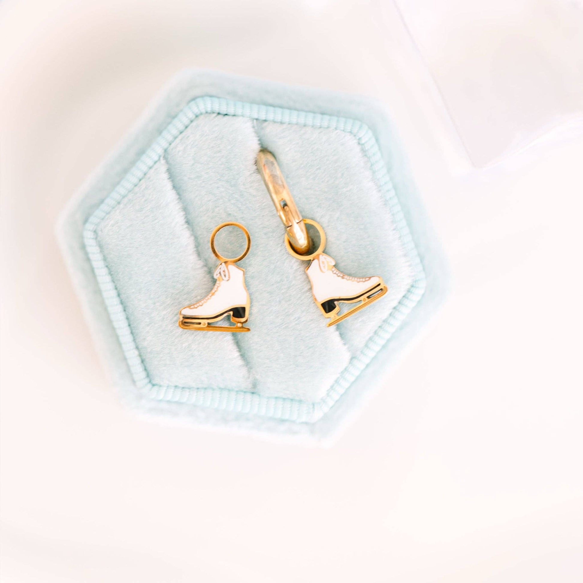 Gold ice skate earrings on a light blue hexagonal jewelry box