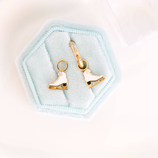 Gold ice skate earrings on a light blue hexagonal jewelry box