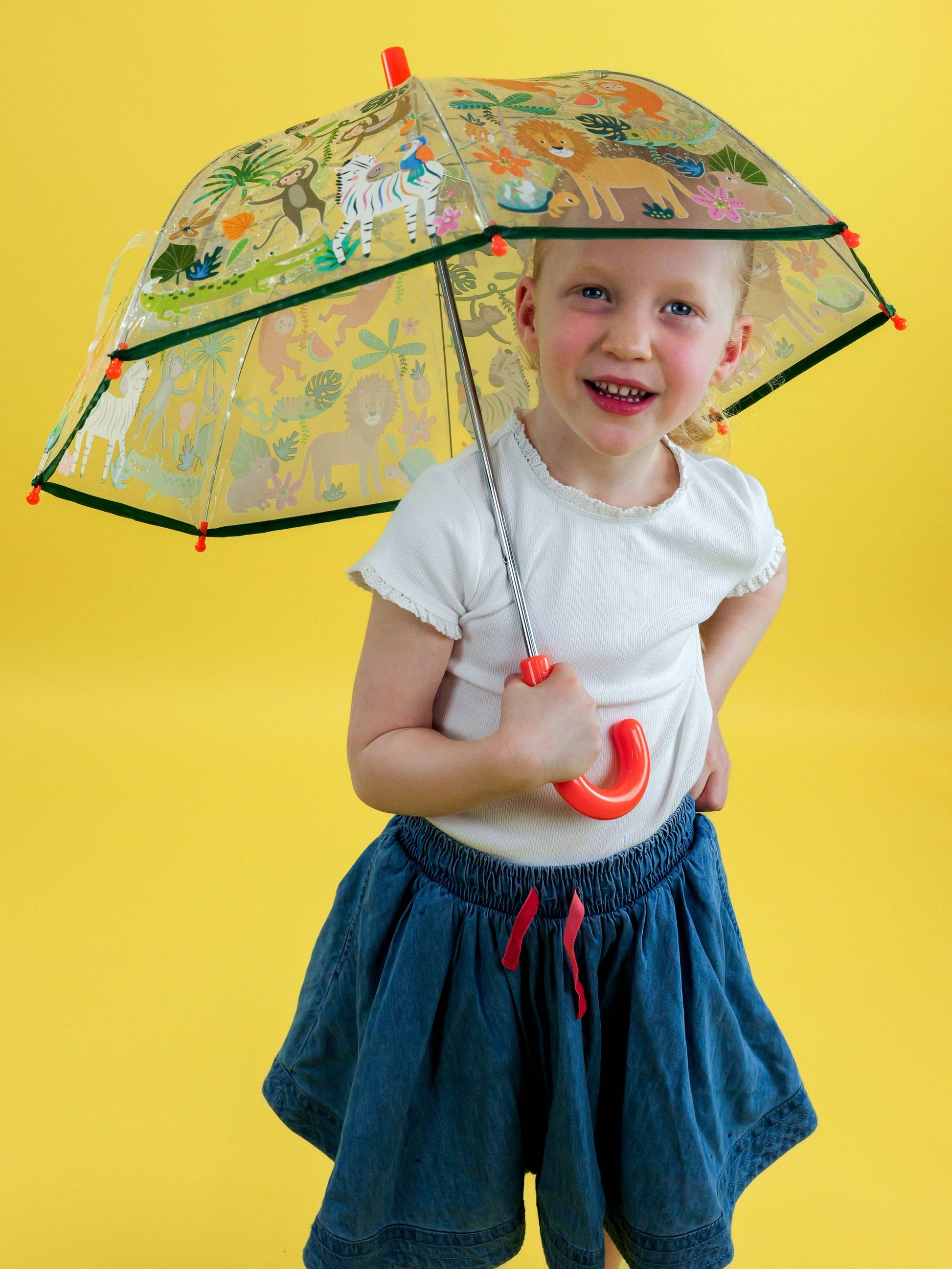 Child holding a transparent umbrella with animal prints against a yellow background