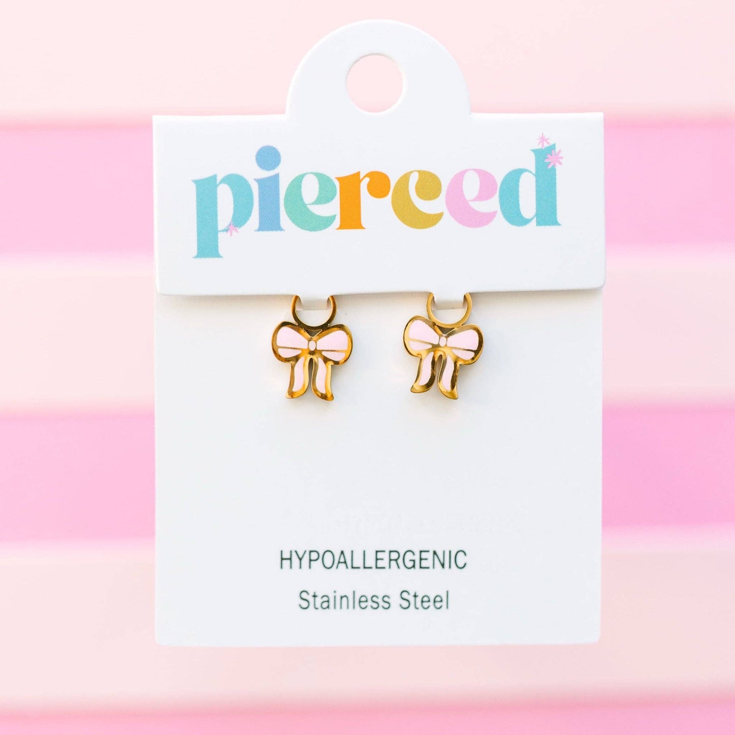 Gold bow-shaped earrings on a 'pierceed' branded card with a pink gradient background