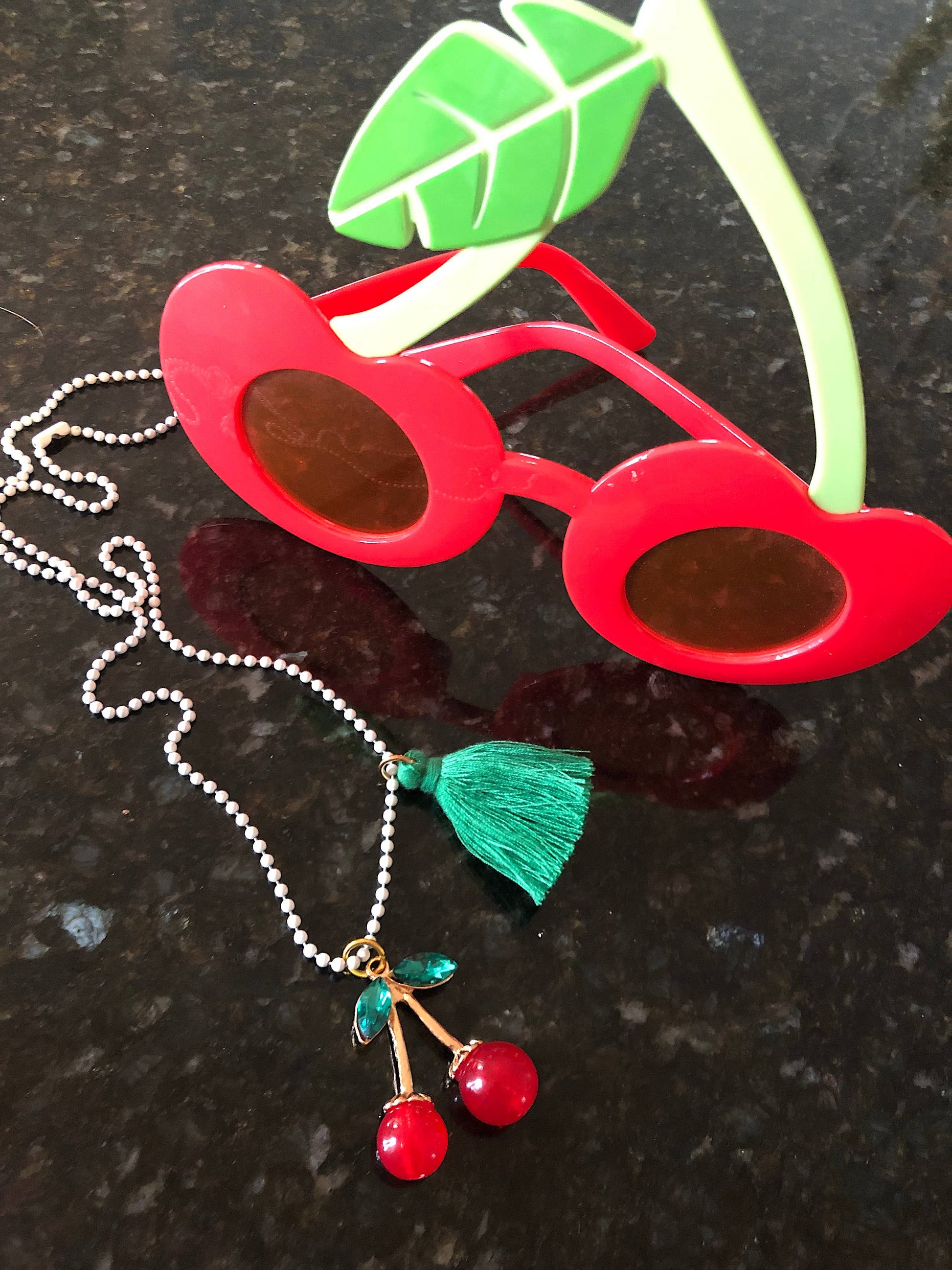 Red sunglasses with a cherry necklace on a dark surface