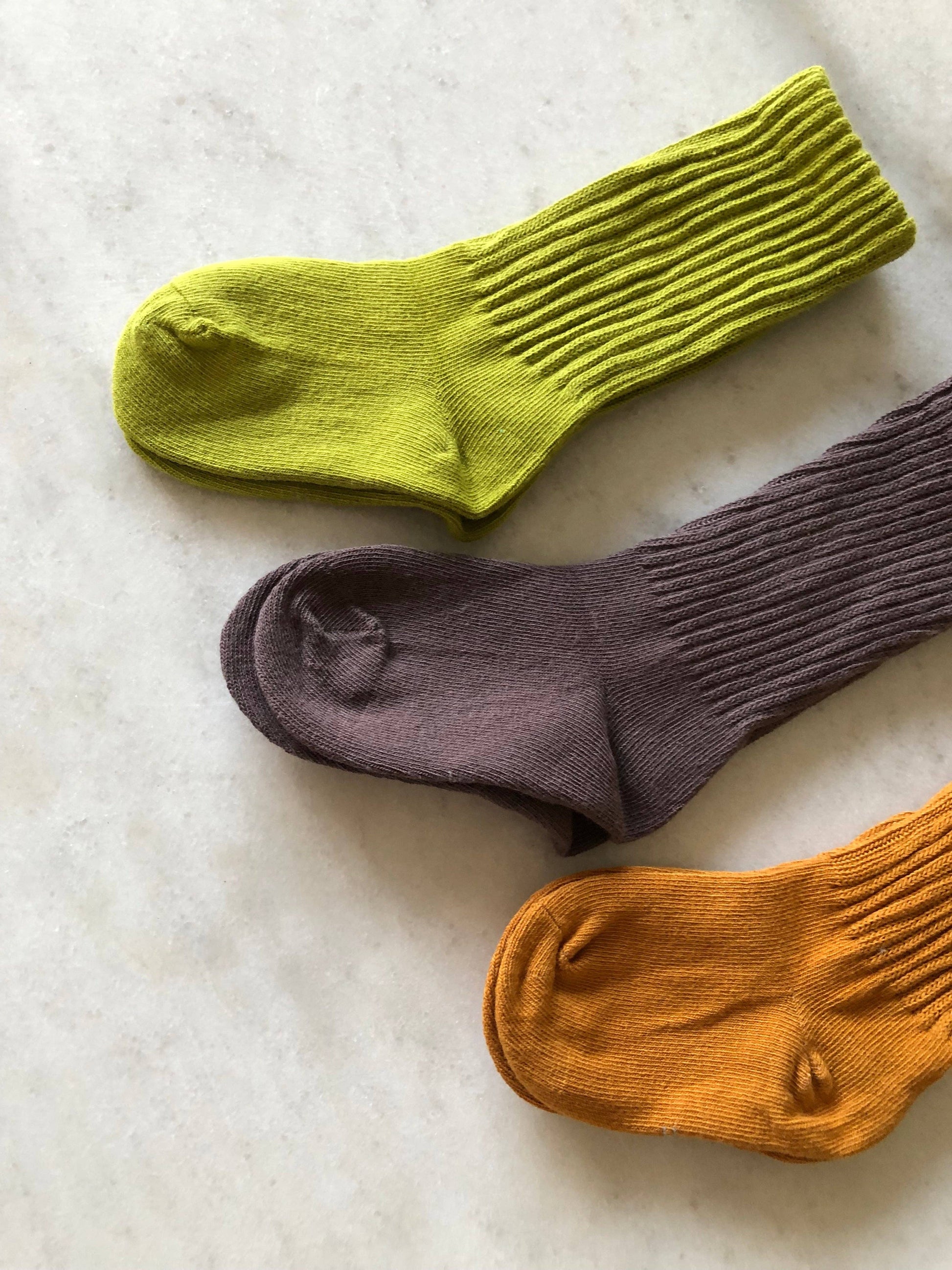 Three socks in green, purple, and orange on a textured surface