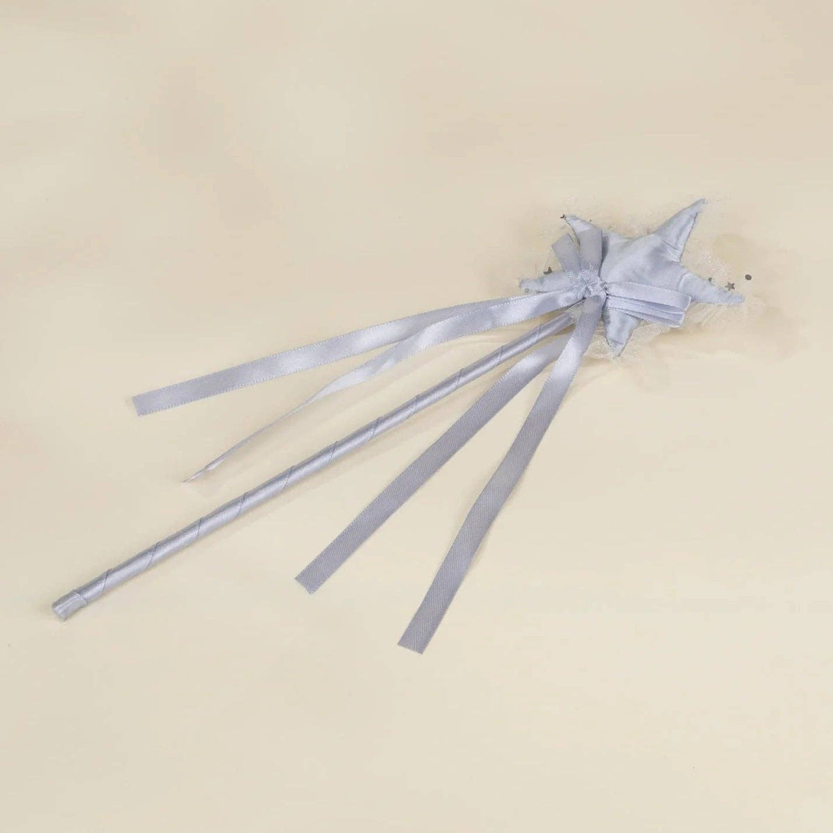 A light silver-gray fabric hair accessory with a small bow and long ribbon tails, laid flat on a warm beige background.