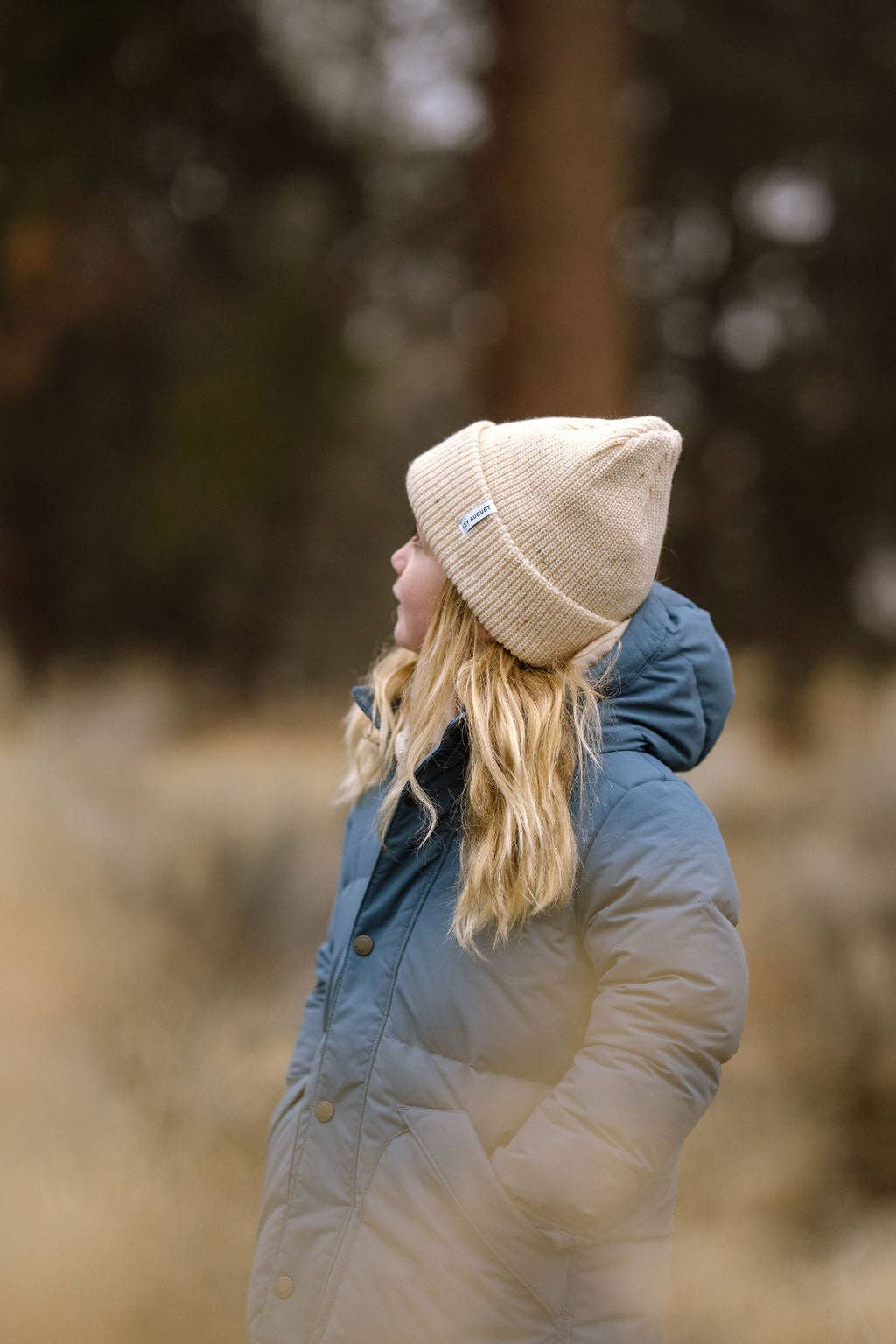 Person wearing a beige beanie and blue jacket in a forest setting