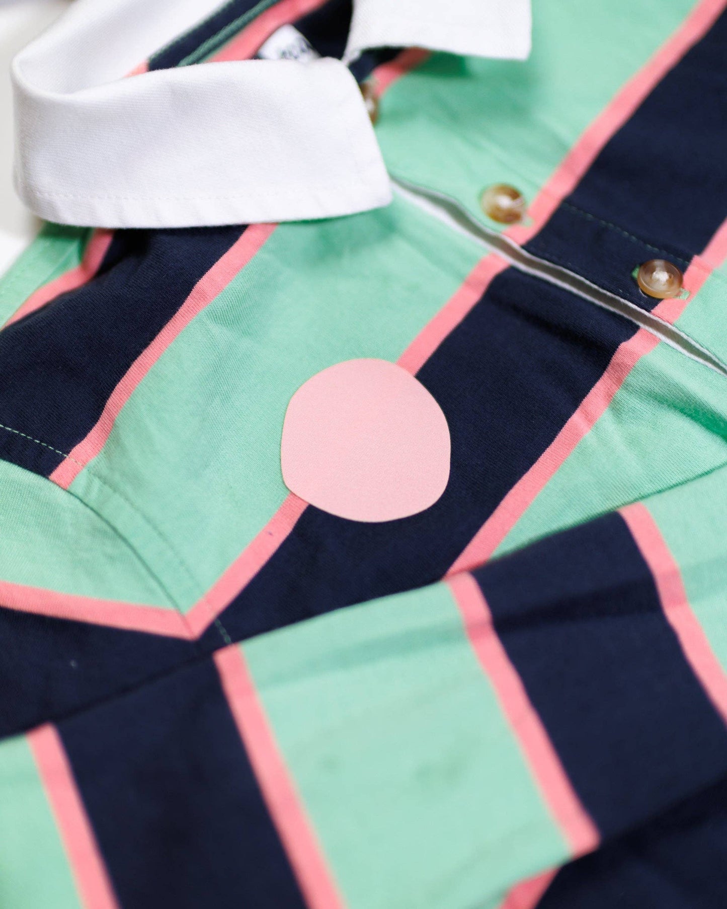 Close-up of a shirt with green, pink, and navy pattern with patch at chest