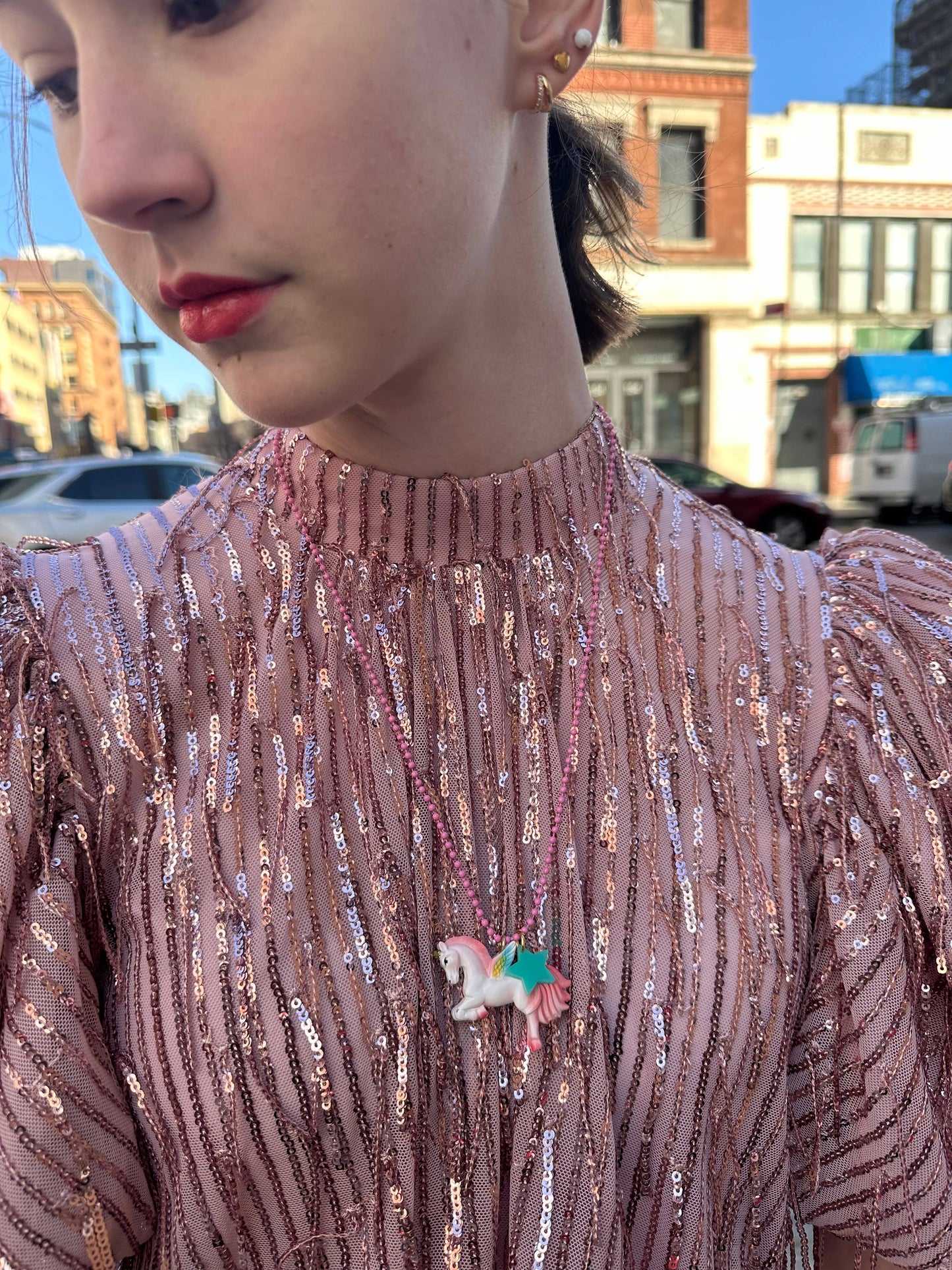 Close-up of a person wearing a pink sequined top with a unicorn brooch, outdoors.