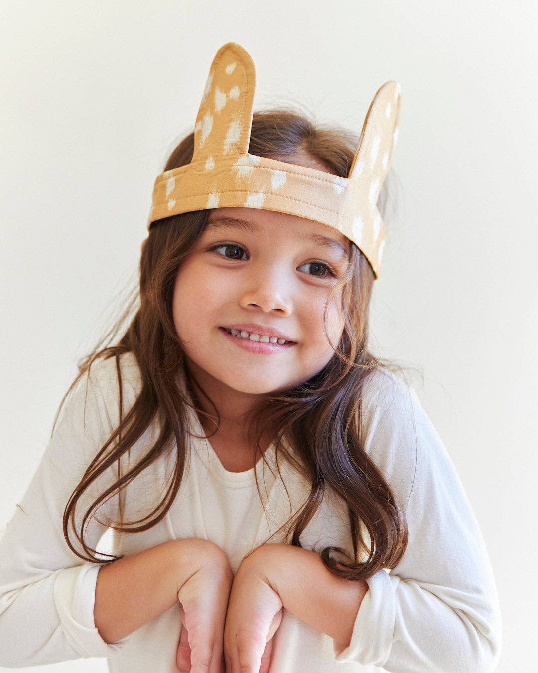 Child wearing a headband with deer ears on a plain background
