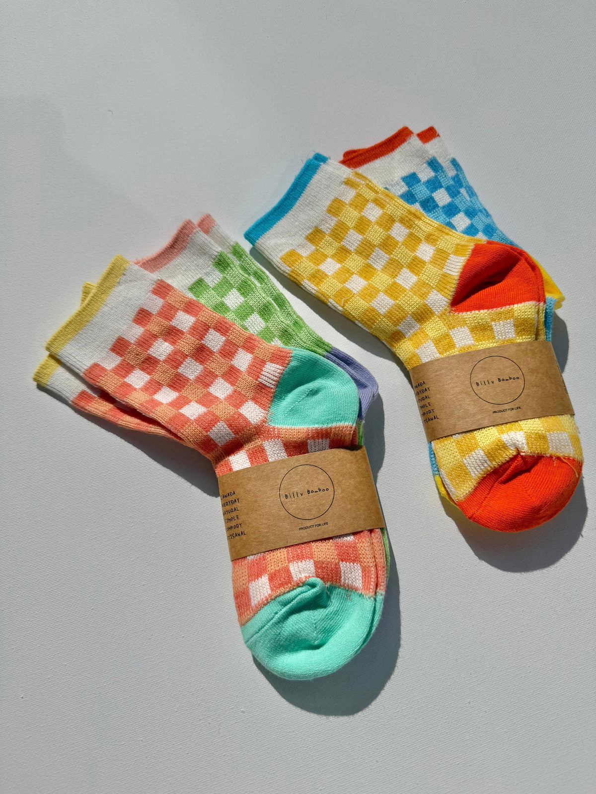 Crew socks with colorful checkered patterns, wrapped in brown paper bands, displayed on a light gray background.