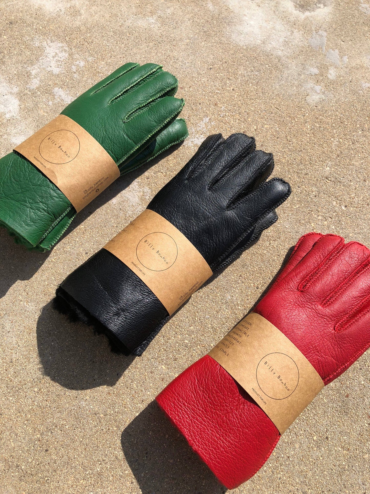 Three pairs of leather gloves in green, black, and red on a textured surface.