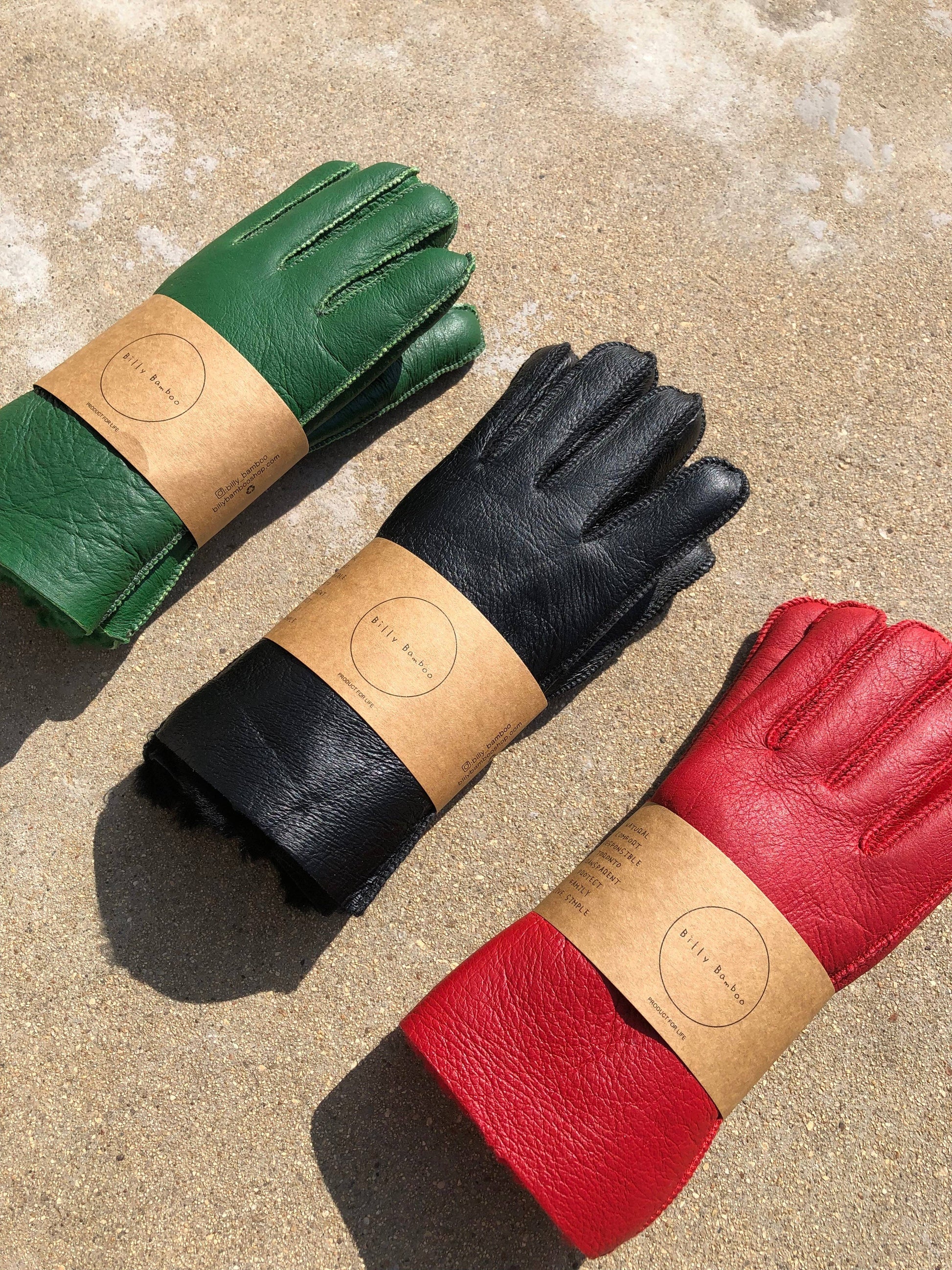 Three pairs of leather gloves in green, black, and red on a textured surface.