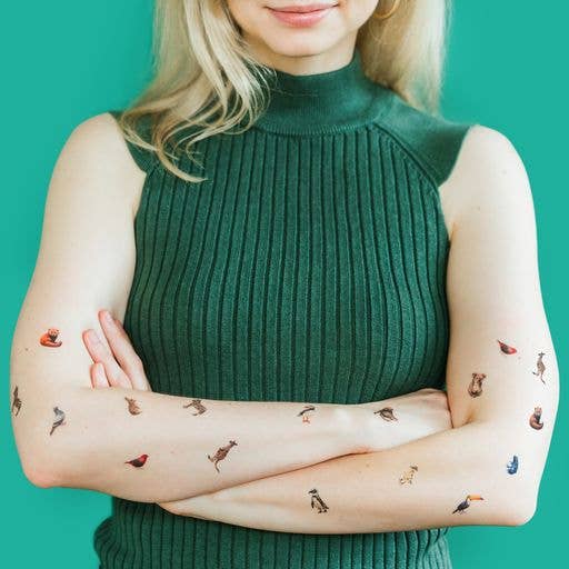 Woman wearing a green sleeveless top with temporary tattoos on her arms against a teal background