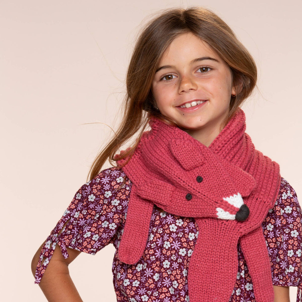 Young girl wearing a pink knitted scarf with a cat design on a beige background