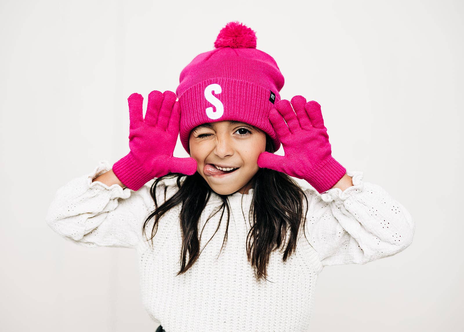 Child wearing a pink beanie with a pom-pom and matching gloves on a white background