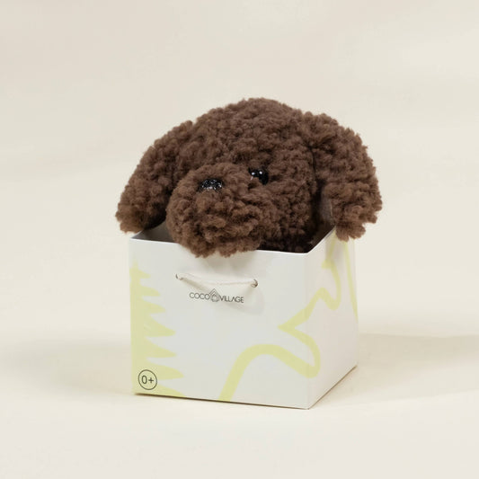 Brown plush dog toy inside a white box with yellow text on a beige background