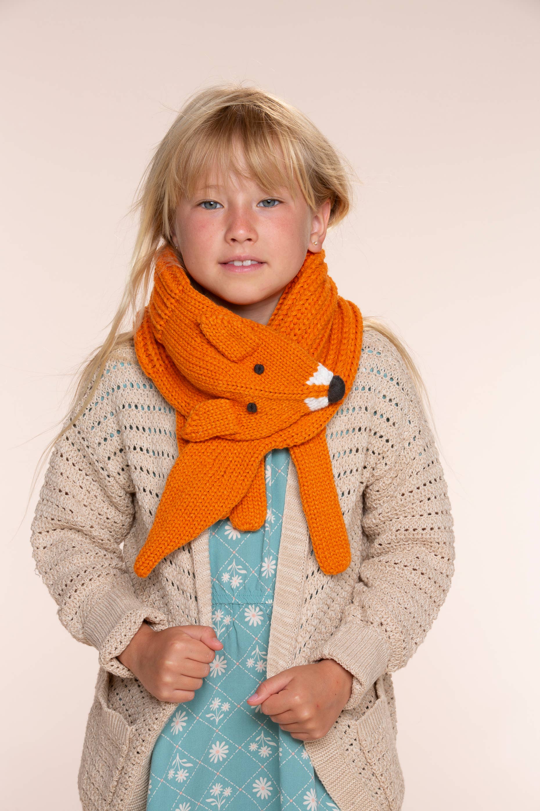 Child wearing a large orange knitted scarf with a white background