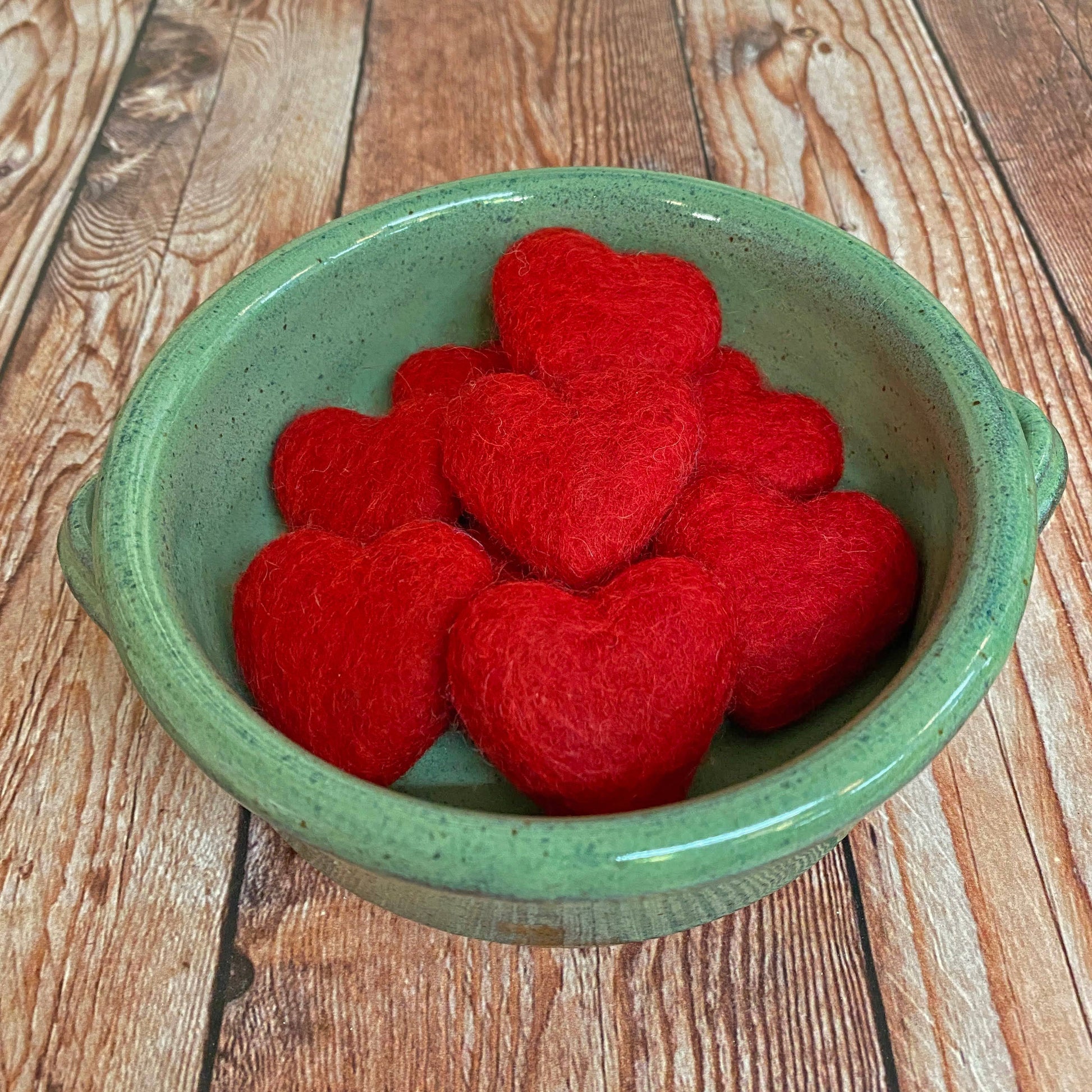 Red heart-shaped objects in a green bowl on a wooden surface