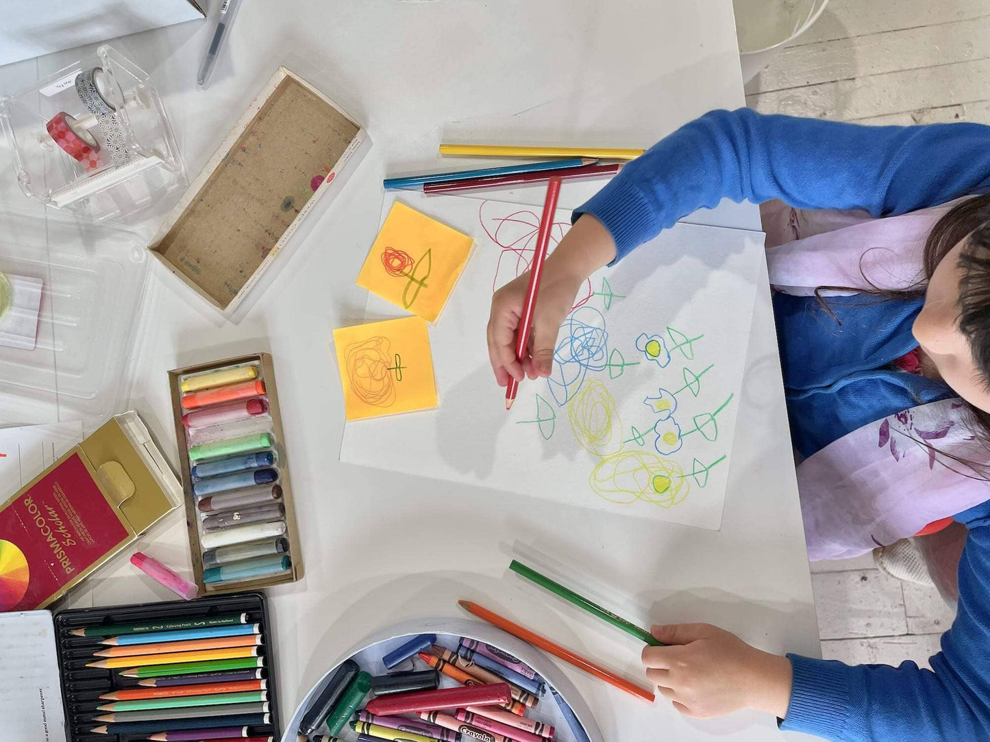 Child drawing with colored pencils on a table with art supplies