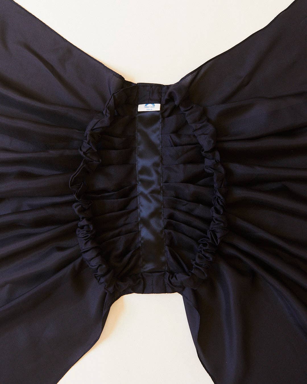 Close-up of a black silk bat-wing costume accessory with ruffled trim, laid flat on a light beige background.