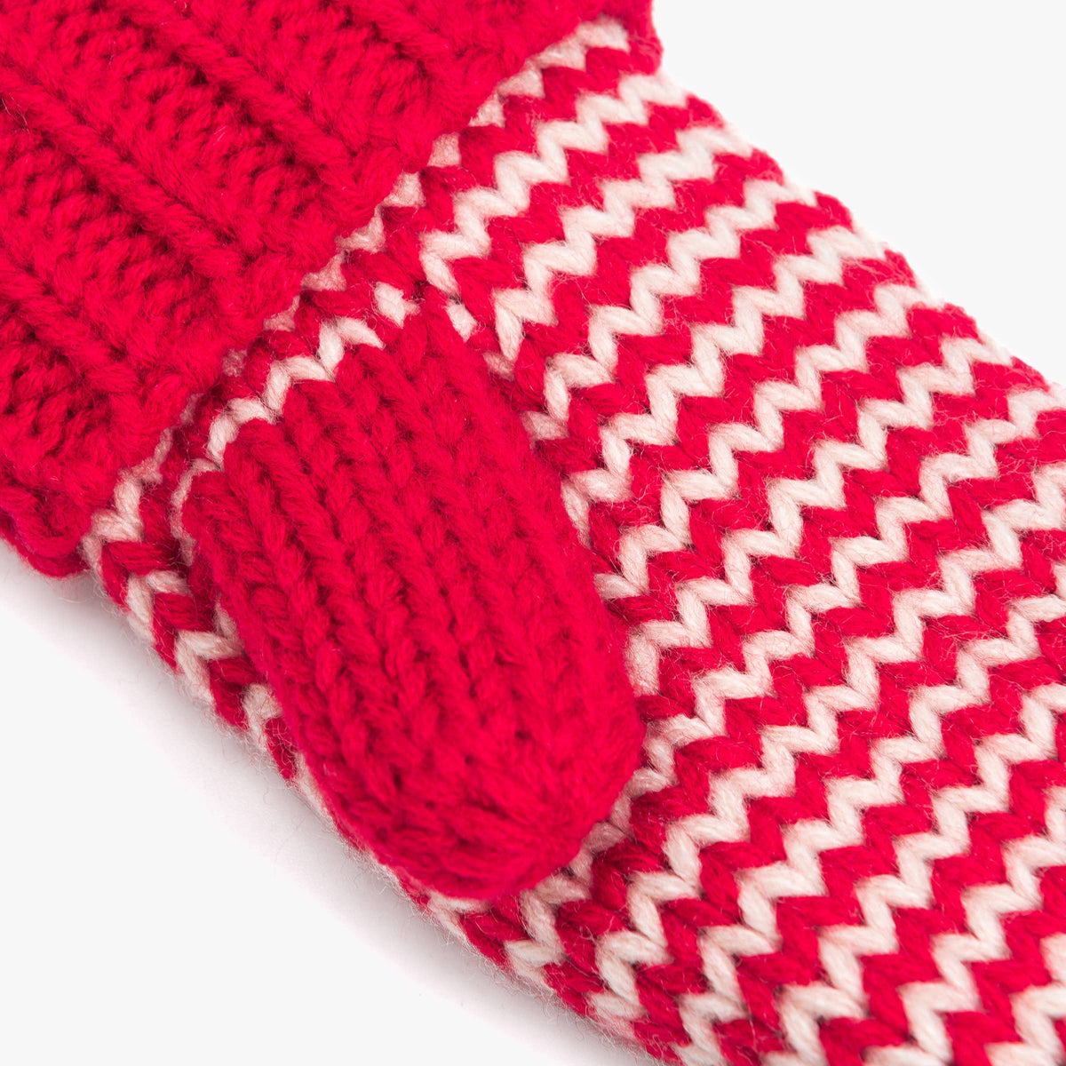 Close-up of a red and white knit accessory, showing a ribbed cuff with a matching red loop tab and a red-and-white chevron pattern on a white background.