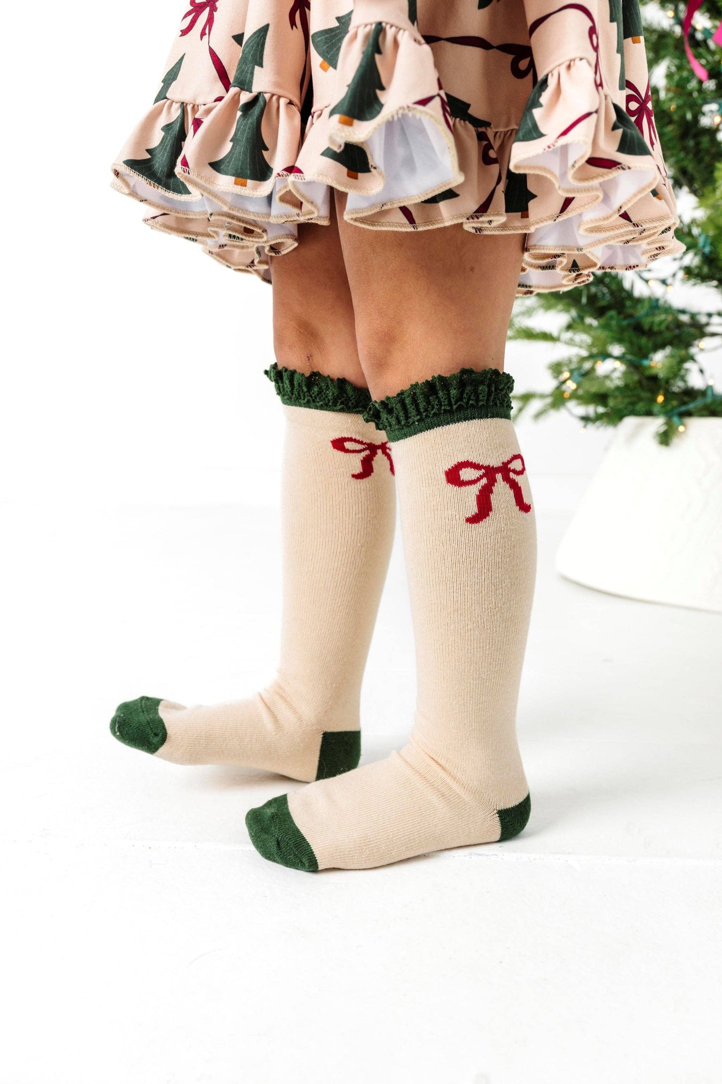 Beige knee-high socks with green accents and red bows worn with a festive dress.