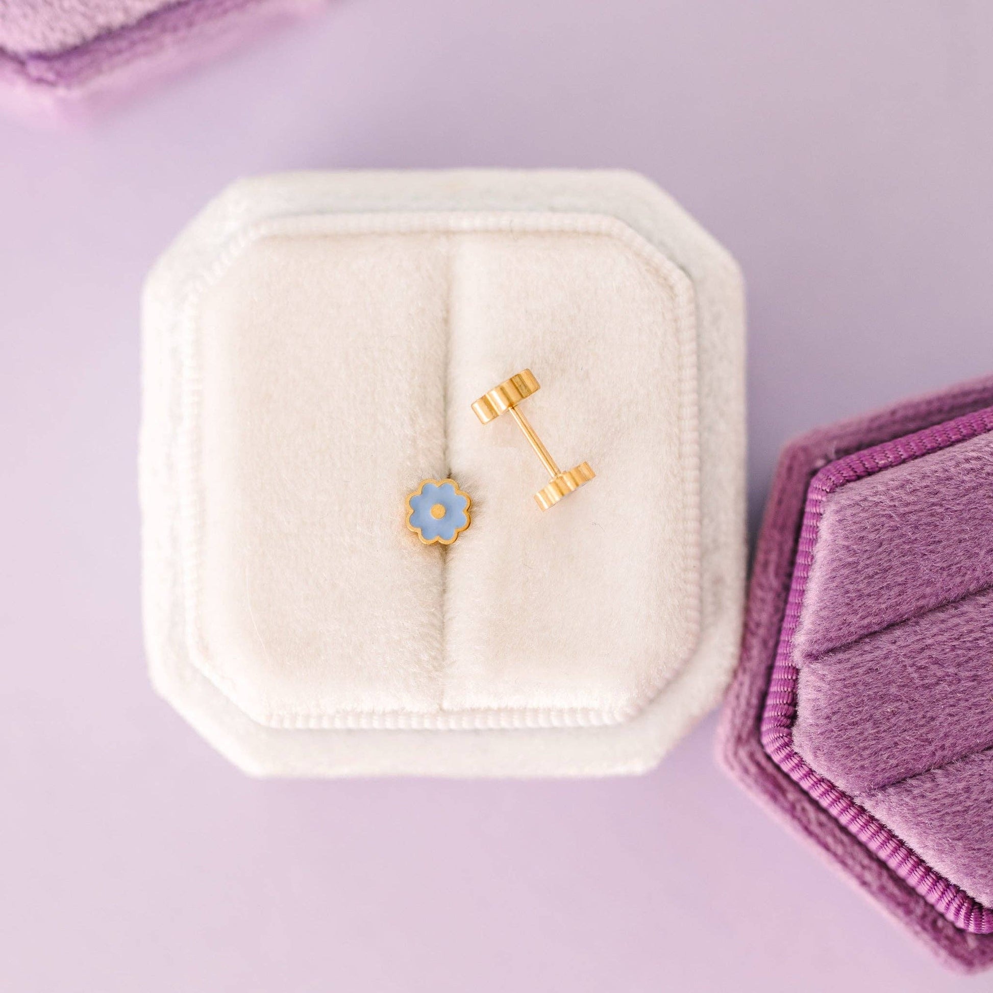 Two earrings in a white jewelry box on a purple background