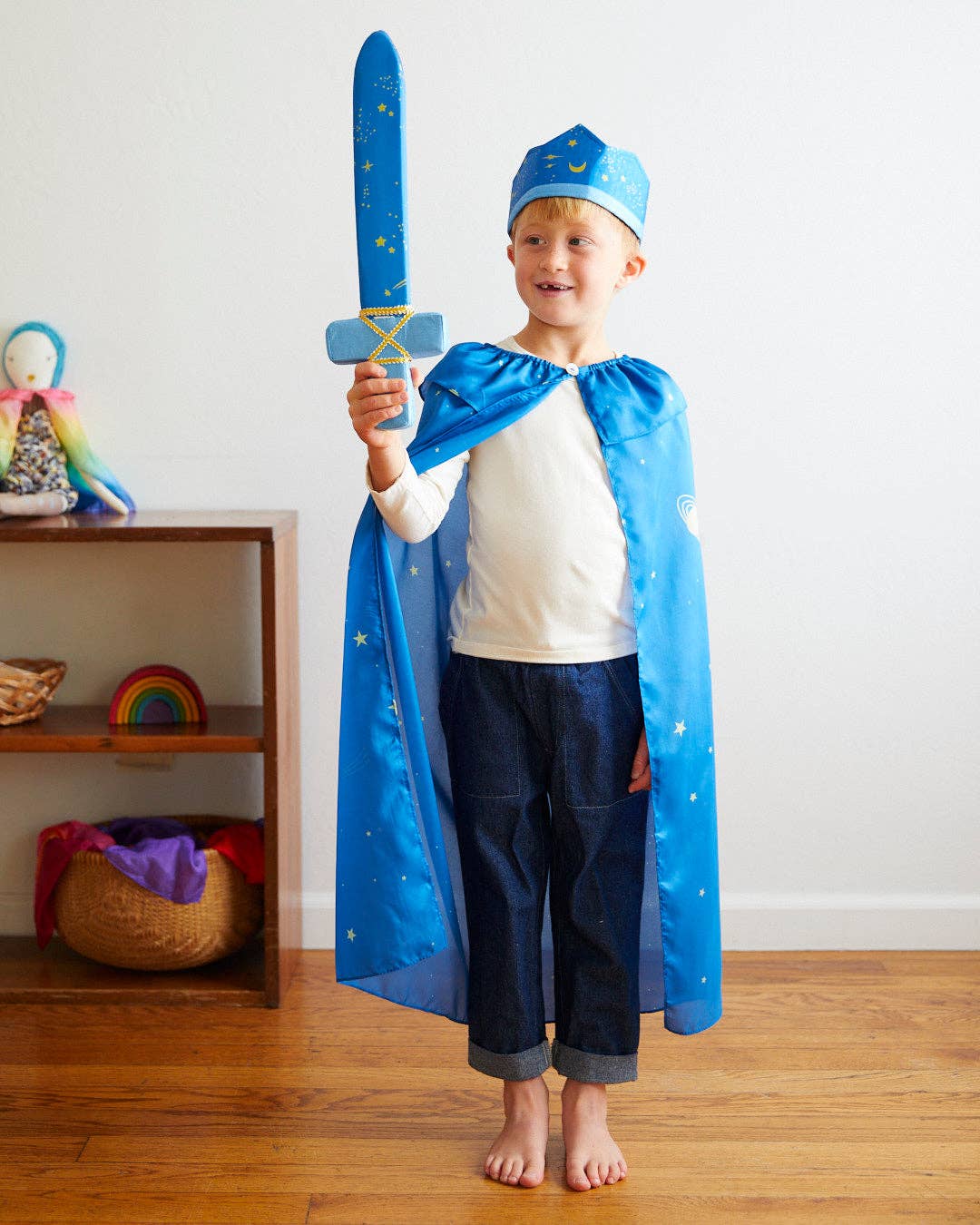 Child in a blue superhero costume holding a toy sword in a room with a shelf and colorful items.