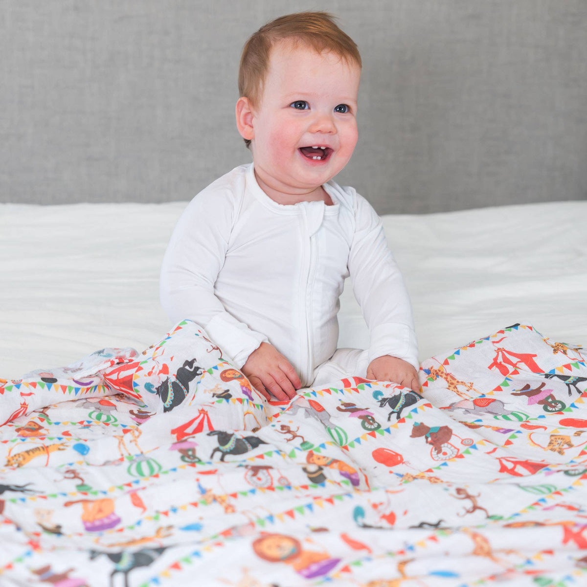 Baby sitting on a bed with a colorful animal-patterned blanket