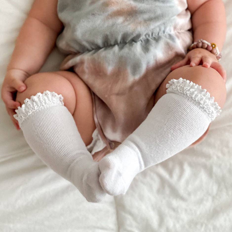 Baby wearing white socks with lace tops on a soft surface