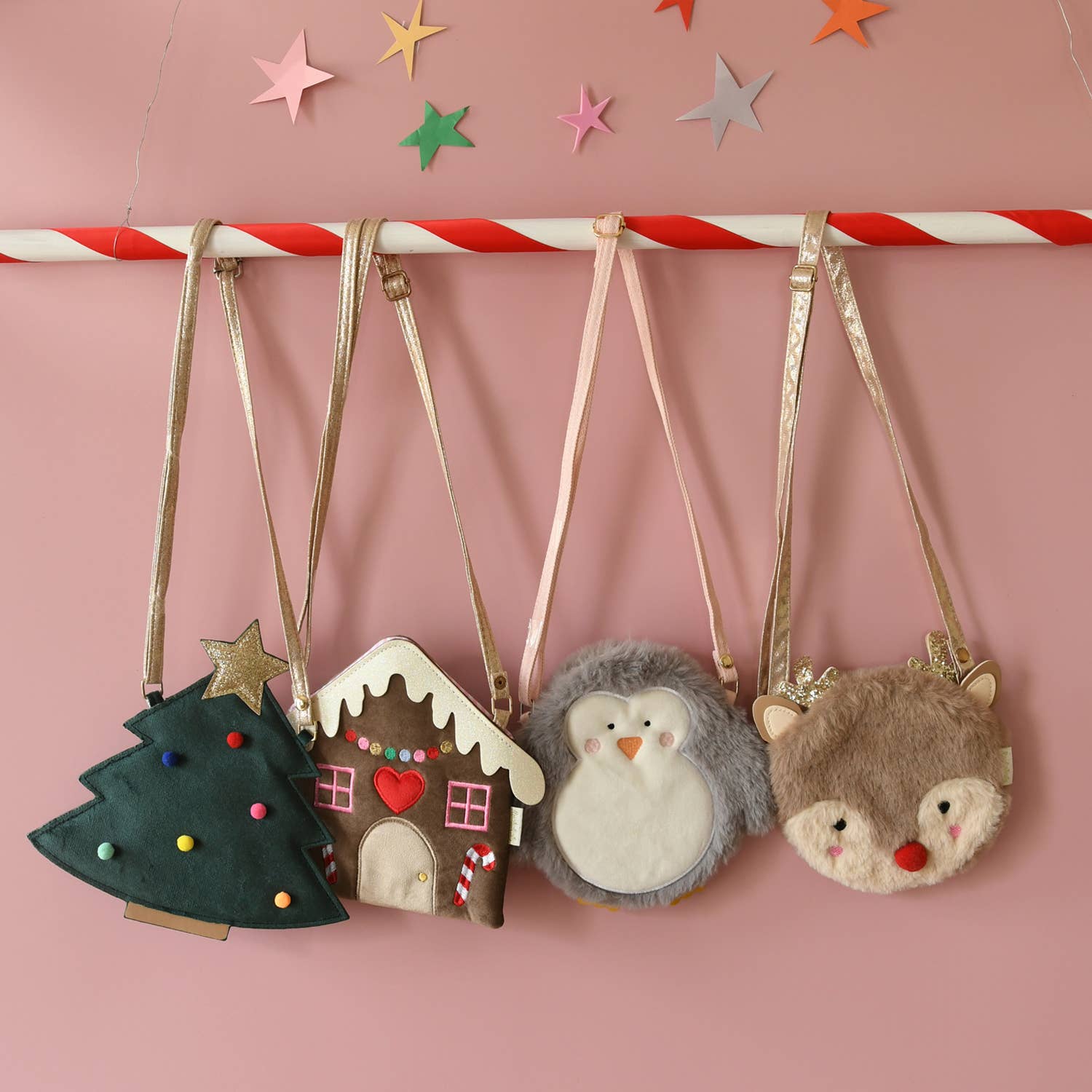 Set of small felt bags shaped like a Christmas tree, gingerbread house, penguin, and deer on a pink background with star decorations.