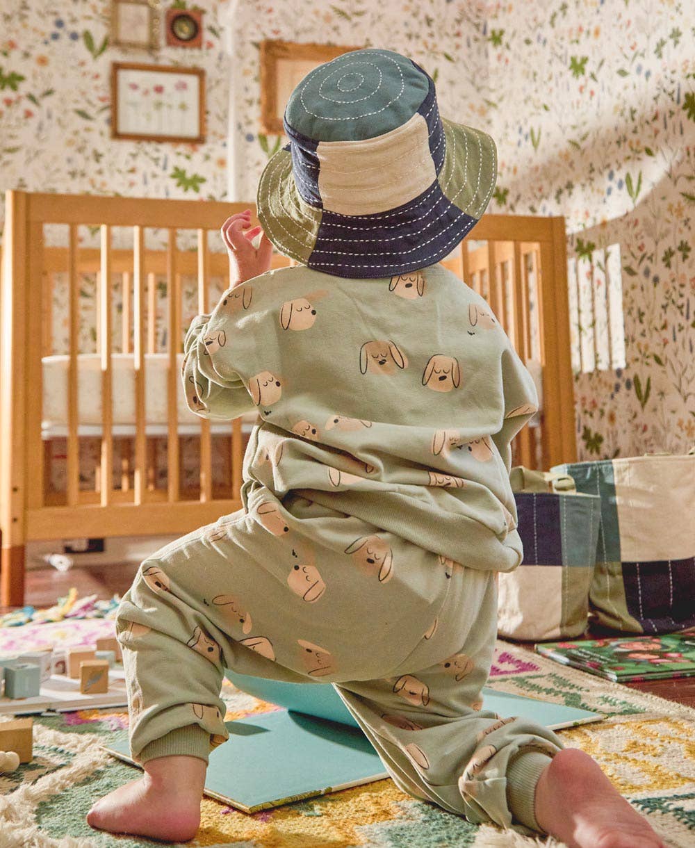 Child wearing a patterned outfit and hats in a nursery setting